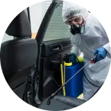 a man in ppe kit spraying chemical in a car for infection from covid and other viruses